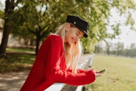 cheerful-blonde-girl-smiling-happily-autumn-park-pretty-woman-looking-her-phone-yellow-trees